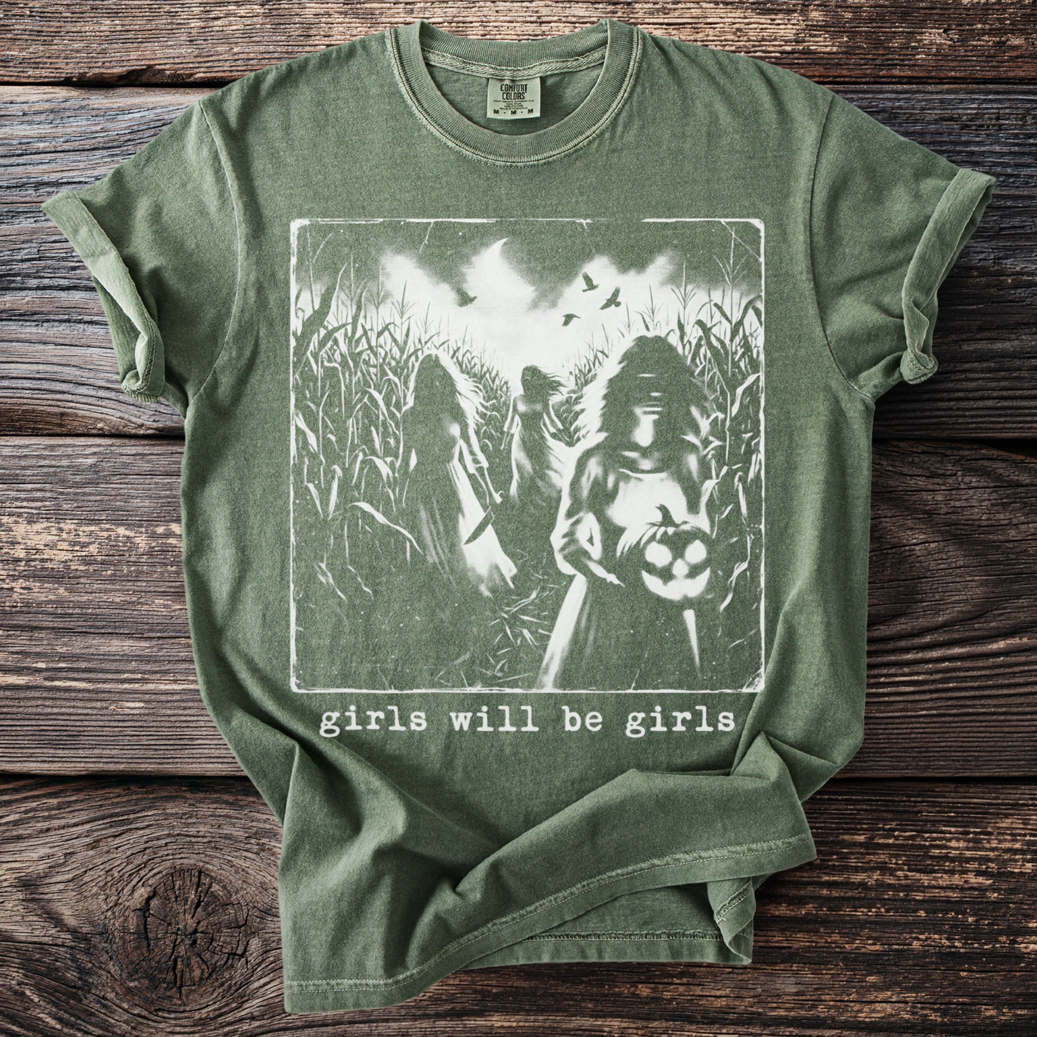 Green t-shirt with spooky girls in a cornfield and "girls will be girls" text.