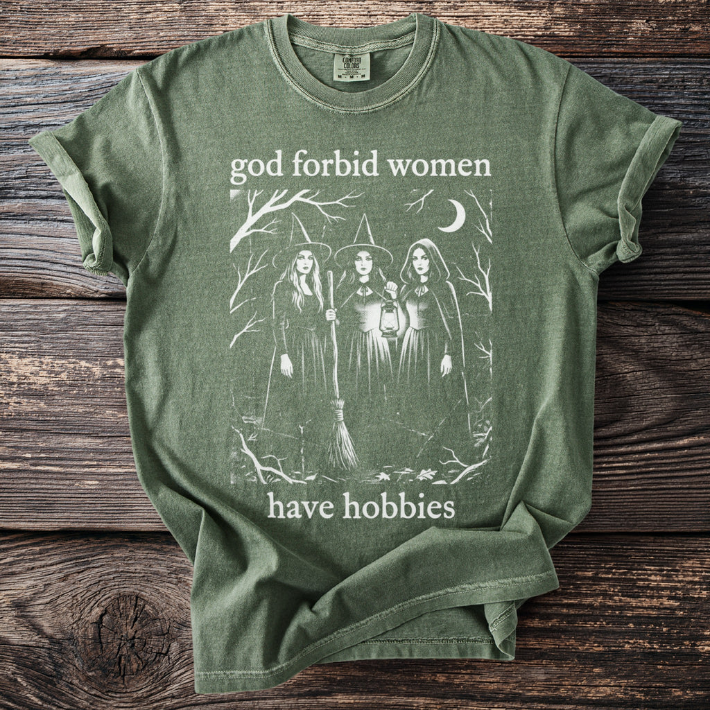 Green t-shirt with white graphic of three witches and text "god forbid women have hobbies".