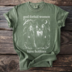 Green t-shirt with white graphic of three witches and text "god forbid women have hobbies".