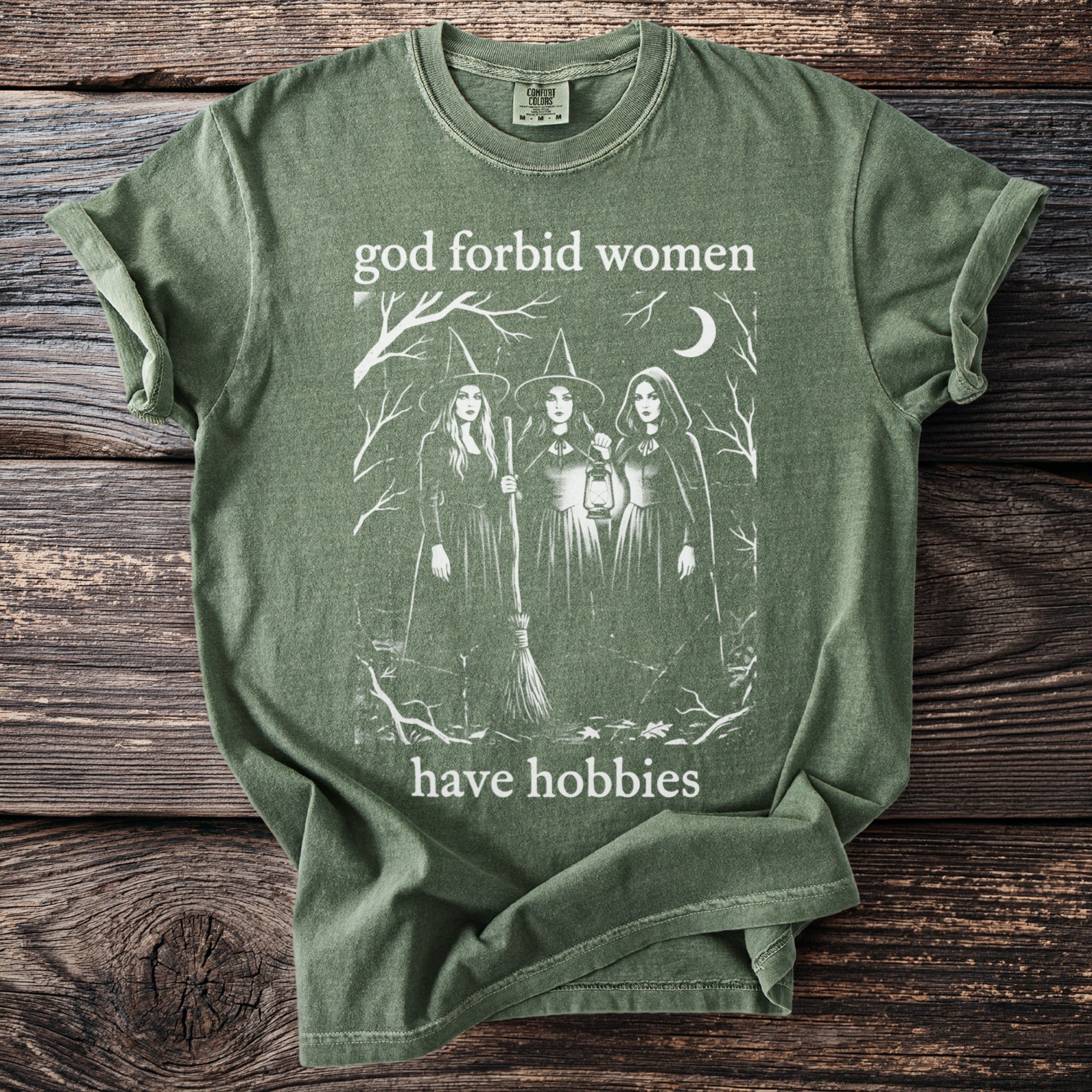 Green t-shirt with white graphic of three witches and text "god forbid women have hobbies".