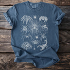 Blue t-shirt with white line drawing of various spiders and a scorpion on a spiderweb.