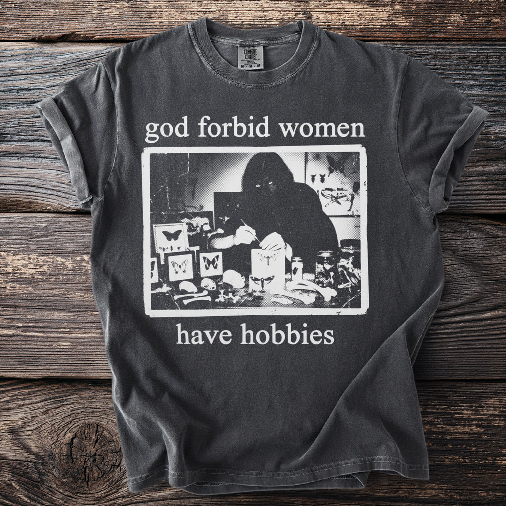 Dark grey t-shirt with "god forbid women have hobbies" and a black and white graphic.