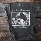 Dark grey t-shirt with "god forbid women have hobbies" and a black and white graphic.