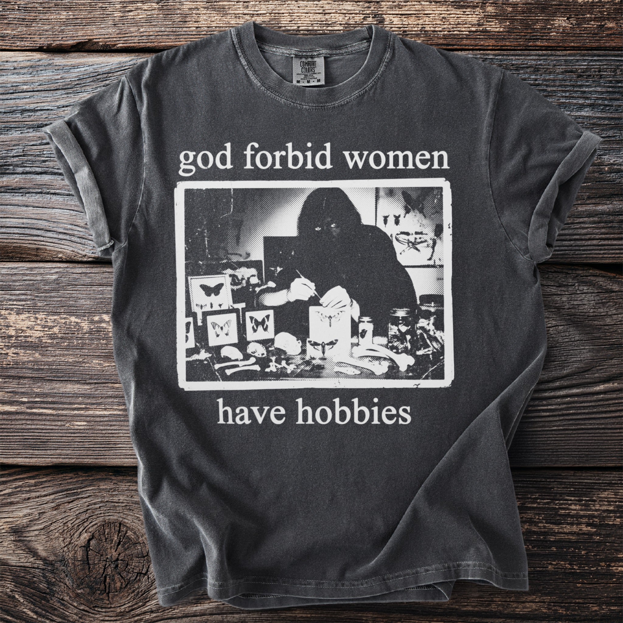 Dark grey t-shirt with "god forbid women have hobbies" and a black and white graphic.