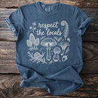 Blue t-shirt with cream graphic of mushrooms, snail, fern, and text "respect the locals".