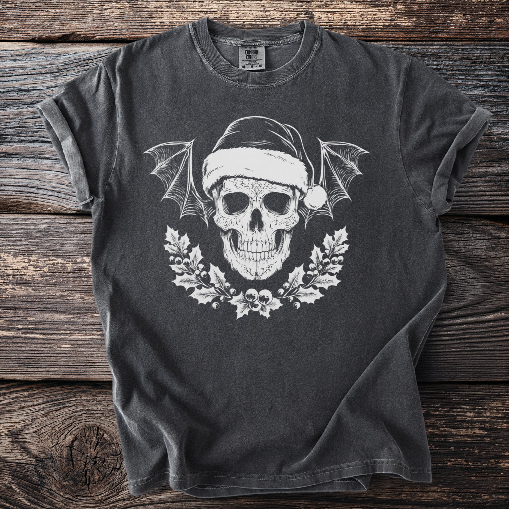 Dark t-shirt with white skull wearing Santa hat, bat wings, and holly wreath.