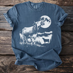 Cow howling at the moon with a smaller cow silhouette in field.