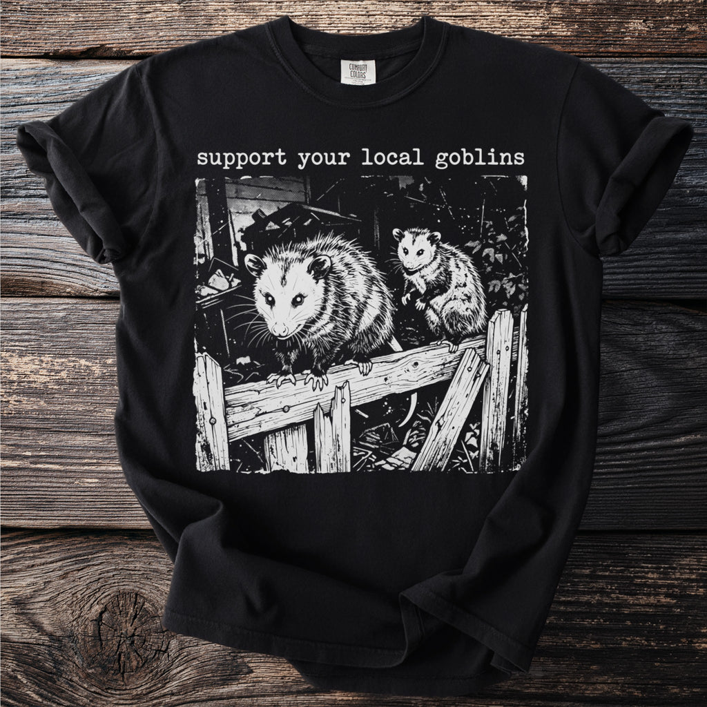 Black t-shirt with "support your local goblins" and opossums on a wooden fence.