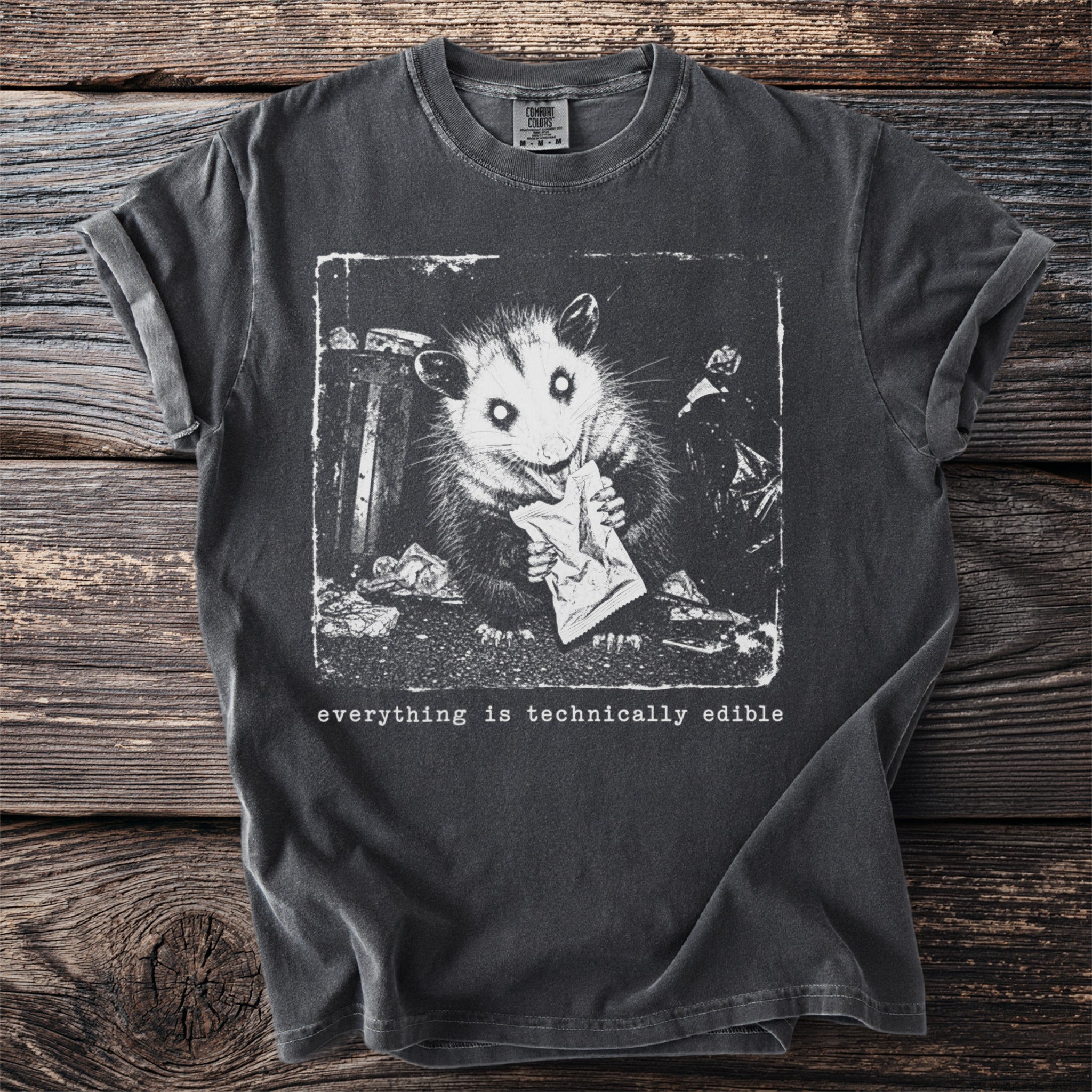 T-shirt with opossum eating from trash and text "everything is technically edible".