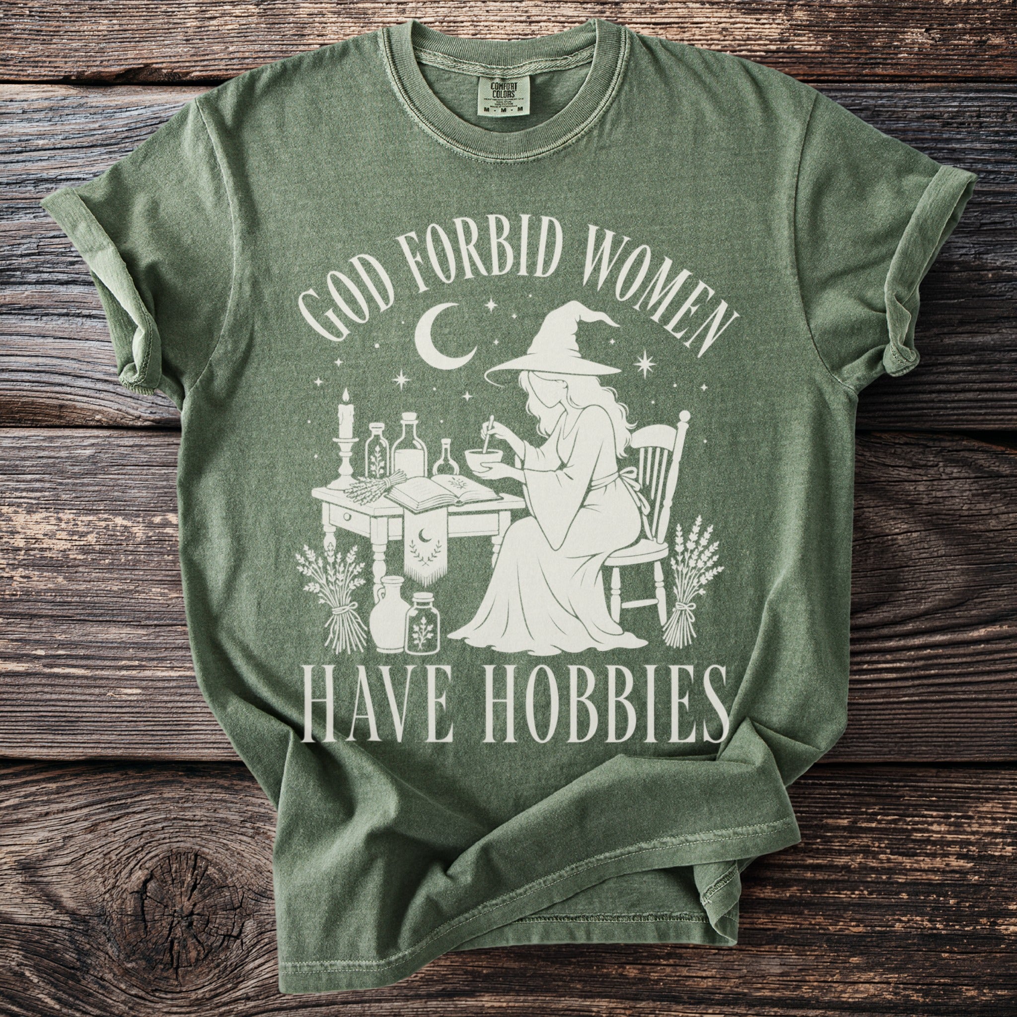 Green t-shirt with "God forbid women have hobbies" text and witch graphic.
