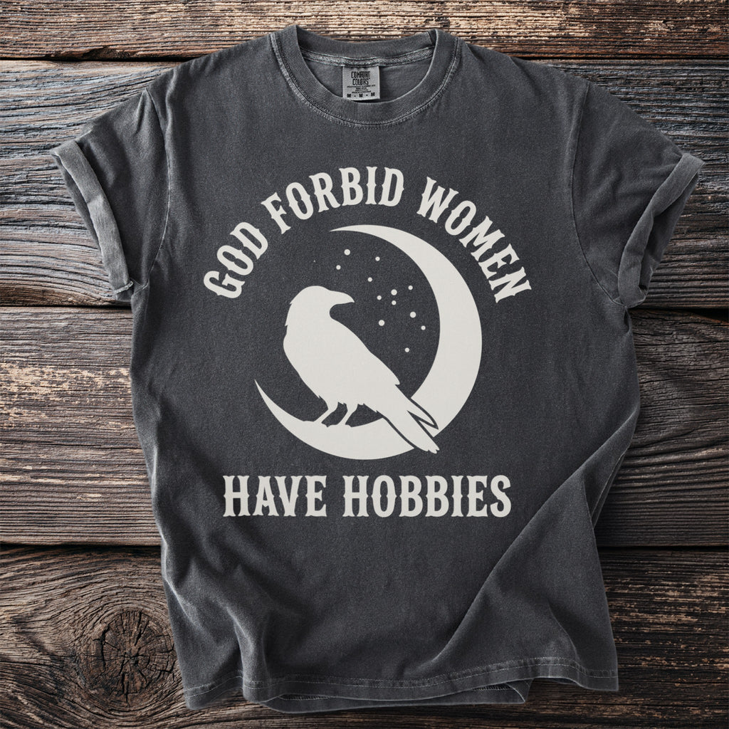 Gray t-shirt with white text and crow graphic on moon: "GOD FORBID WOMEN HAVE HOBBIES"