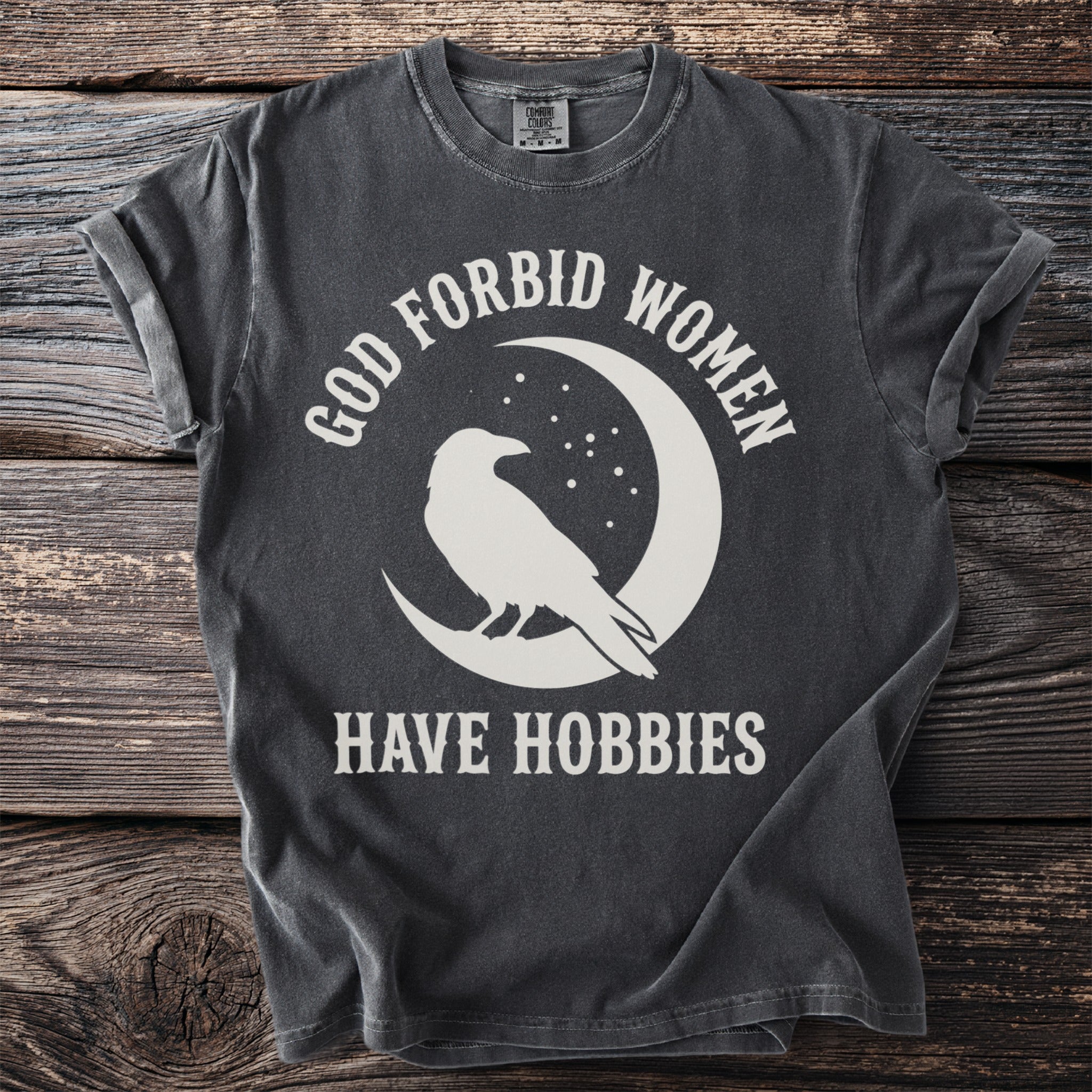 Gray t-shirt with white text and crow graphic on moon: "GOD FORBID WOMEN HAVE HOBBIES"