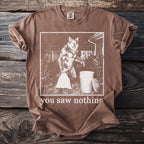 Brown t-shirt with a graphic of a werewolf holding a trash bag next to a trash can and text "you saw nothing".