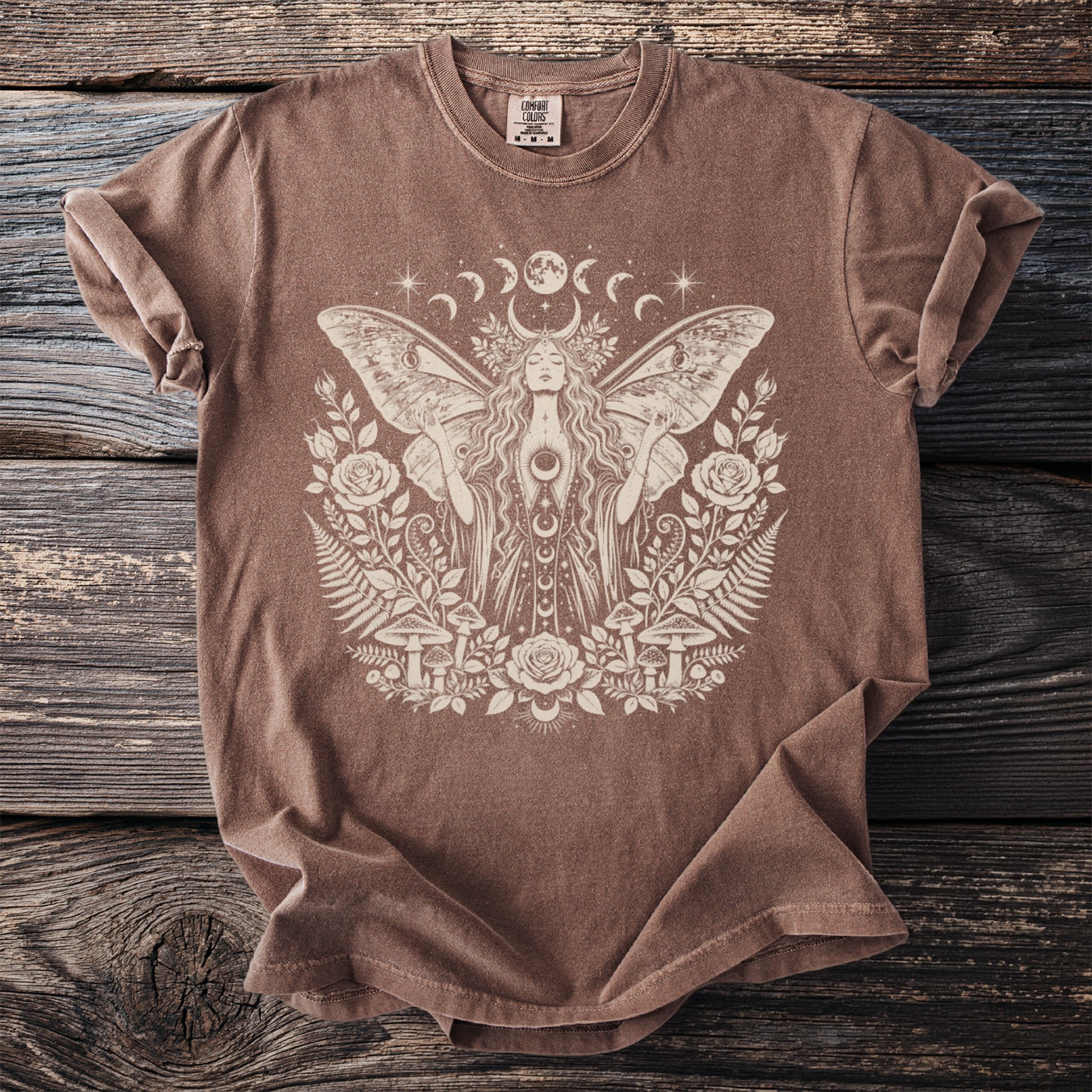 Brown t-shirt with a celestial moth woman graphic surrounded by flora and mushrooms.