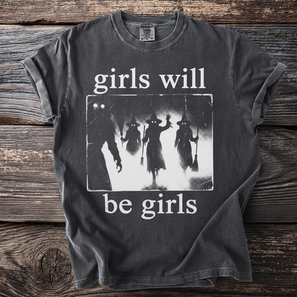 Dark t-shirt with white graphic of silhouettes of three witches and text "girls will be girls."