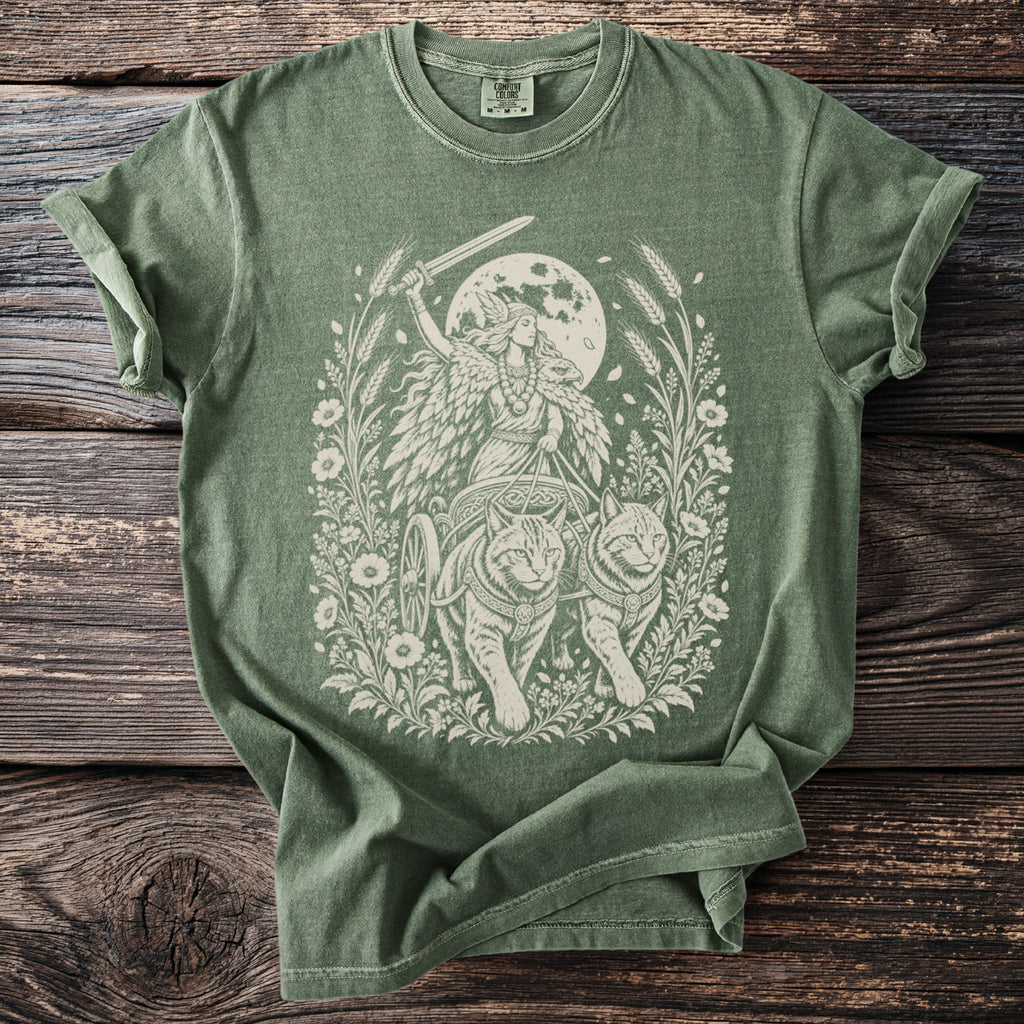 Green t-shirt with a cream print of a winged figure driving a chariot pulled by cats.