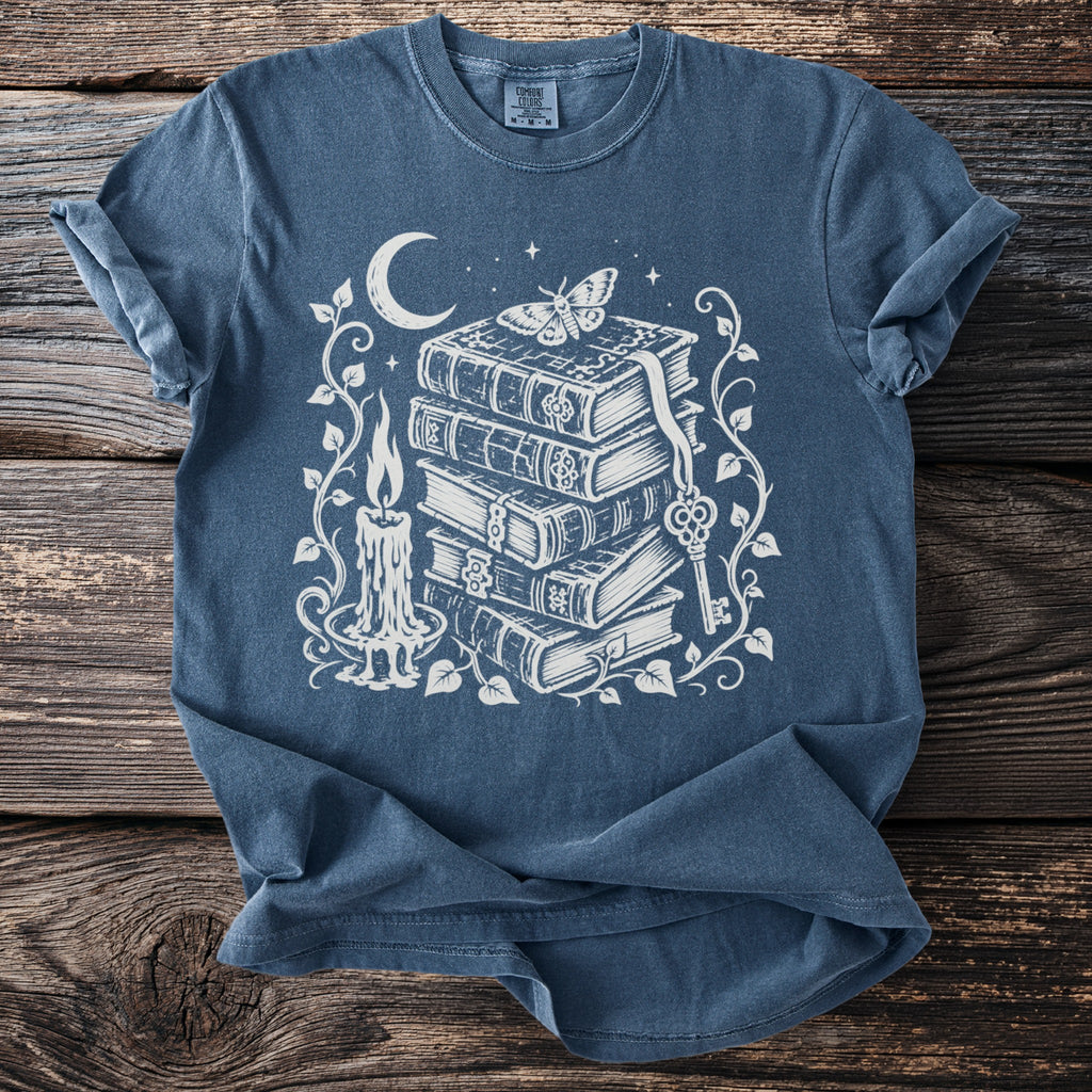 Dark blue t-shirt with white graphic of stacked books, moon, candle, moth, and key.
