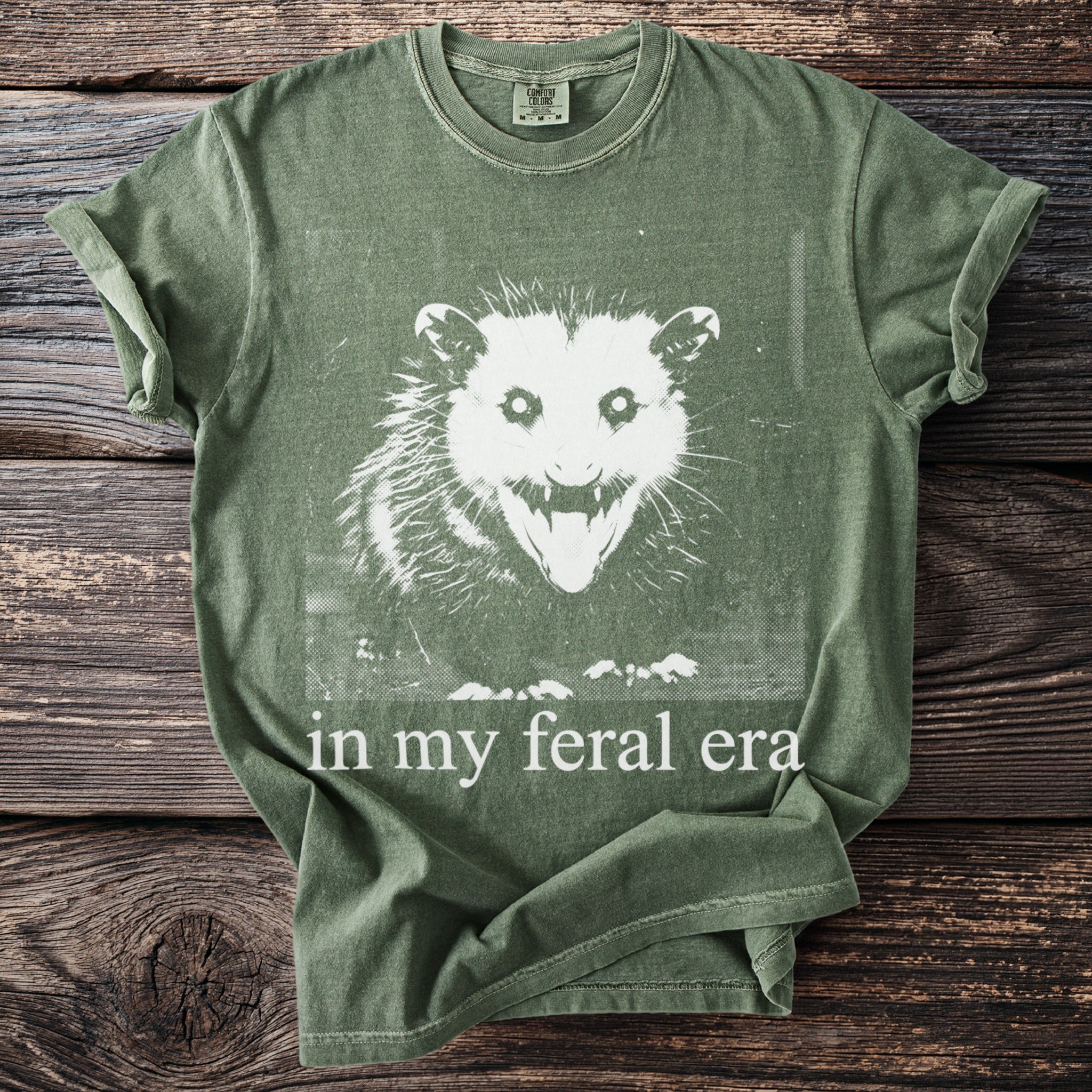 Green t-shirt with white distressed graphic of a possum and text "in my feral era."