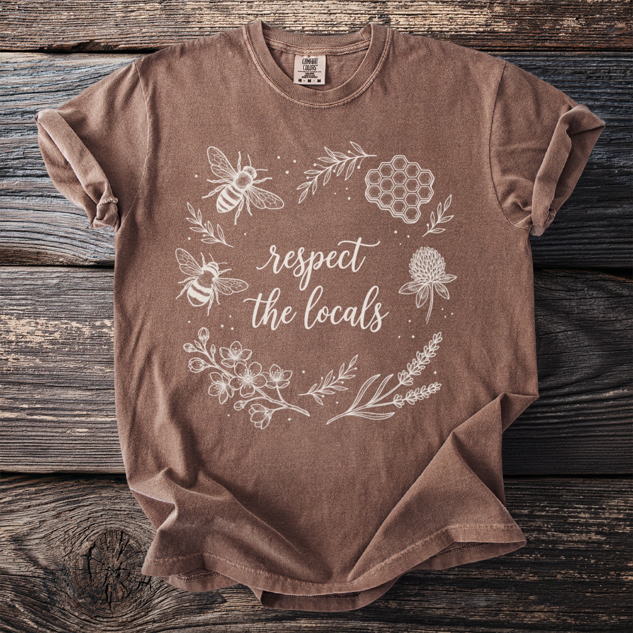 Brown t-shirt with white line art of bees, honeycomb, flowers, and the text "respect the locals".