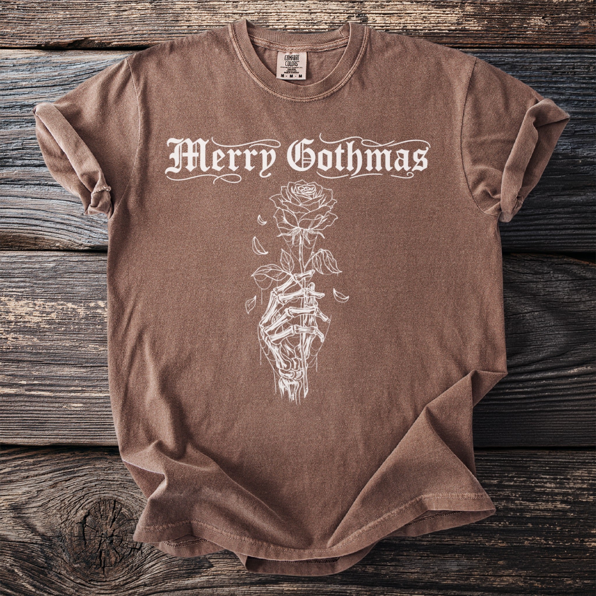 Brown t-shirt with white "Merry Gothmas" text and a skeleton hand holding a rose.