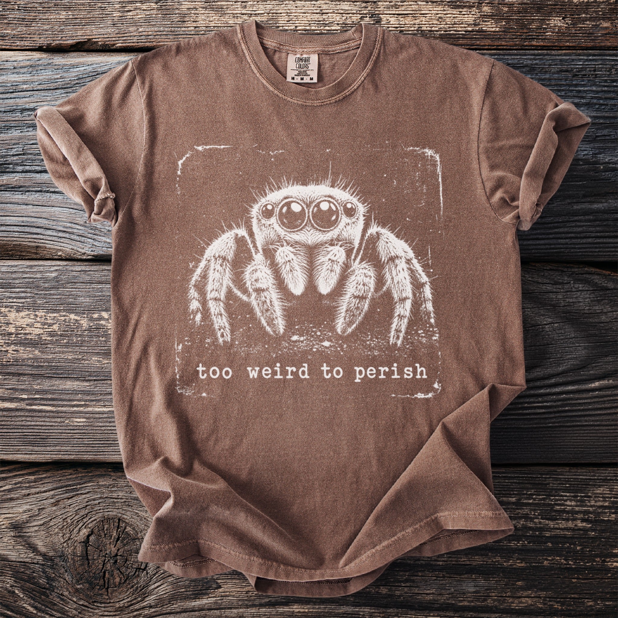 Brown t-shirt with a white graphic of a jumping spider and the text "too weird to perish".