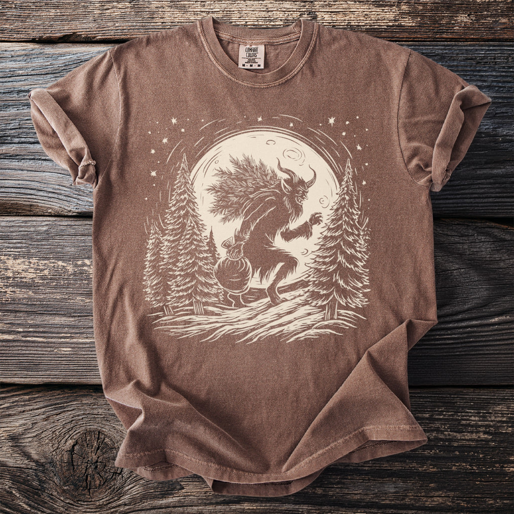 Brown t-shirt with a Krampus graphic carrying a sack and branches under the moon.