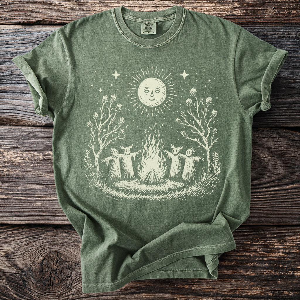 Olive green t-shirt with a cream graphic of a campfire with three figures and a sun.