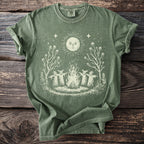 Olive green t-shirt with a cream graphic of a campfire with three figures and a sun.