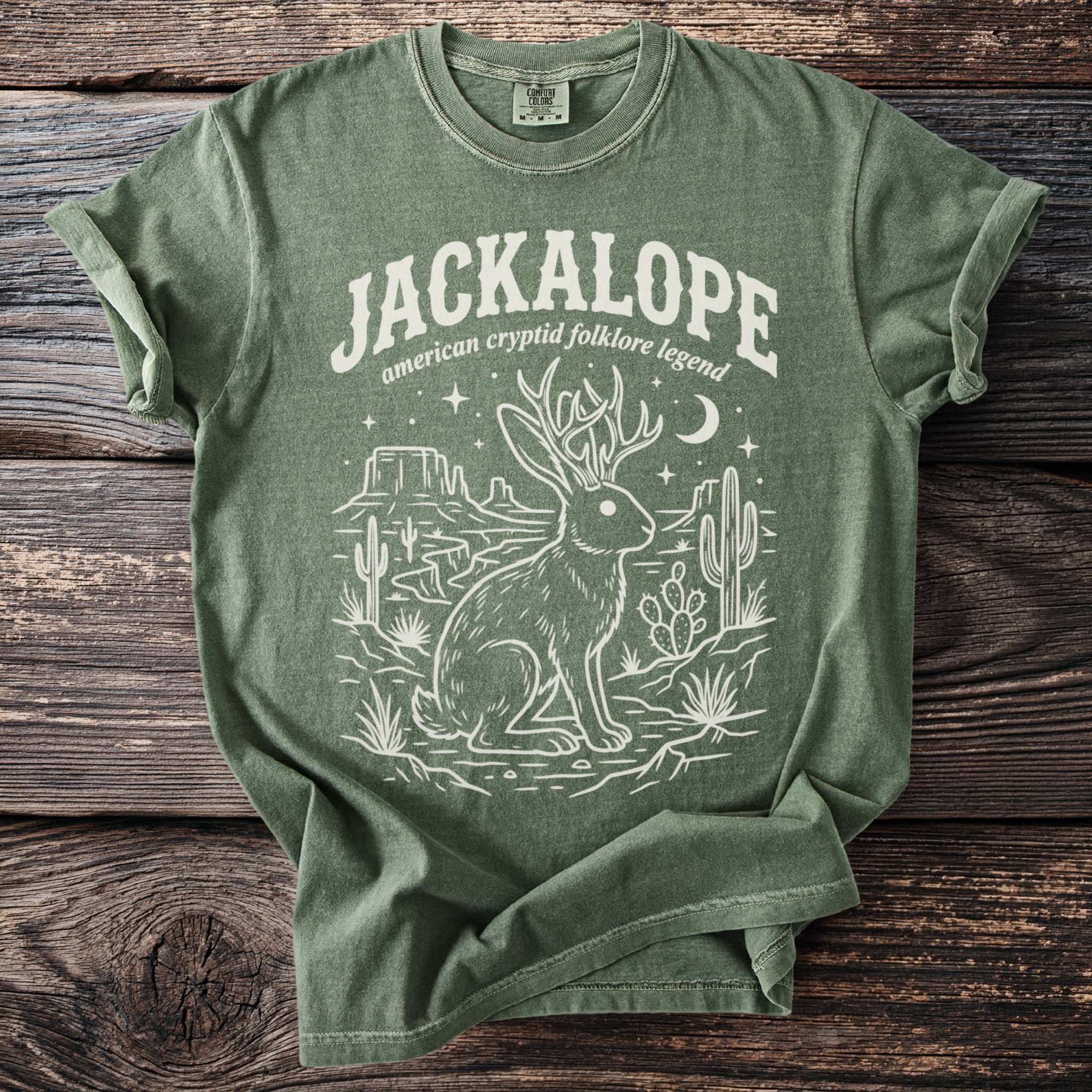Green t-shirt featuring a white line drawing of a jackalope and desert landscape with text.