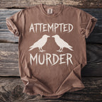 Brown t-shirt with white text "ATTEMPTED MURDER" and two crows.