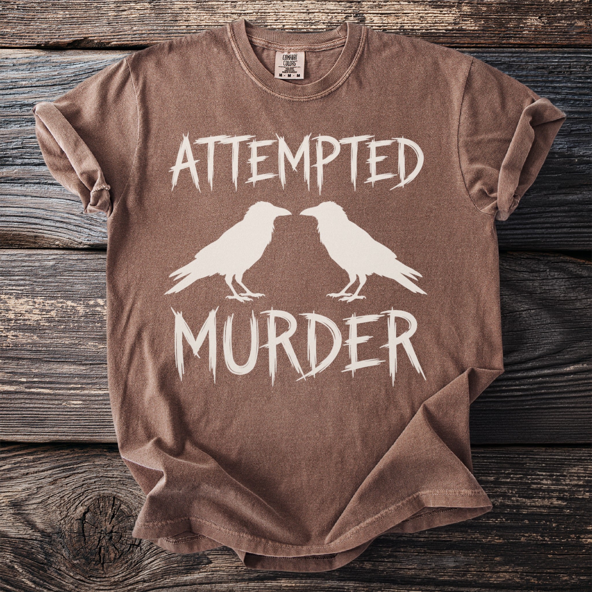 Brown t-shirt with white text "ATTEMPTED MURDER" and two crows.
