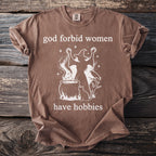 T-shirt with graphic text "god forbid women have hobbies" and witch illustration.