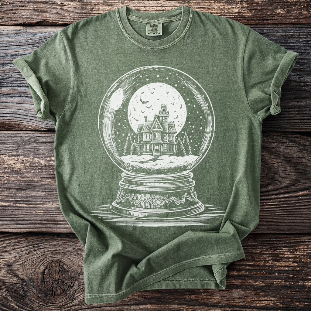 Green t-shirt with a white illustration of a haunted house inside a snow globe.