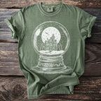 Green t-shirt with a white illustration of a haunted house inside a snow globe.