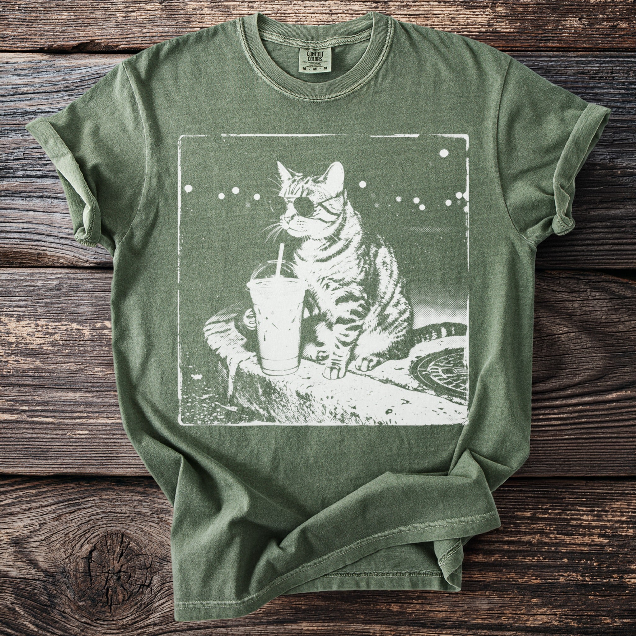 Green t-shirt with white graphic of a cat wearing glasses and an eye patch with a drink.