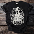 Black t-shirt with a light-colored witchy potion-making graphic and floral accents.