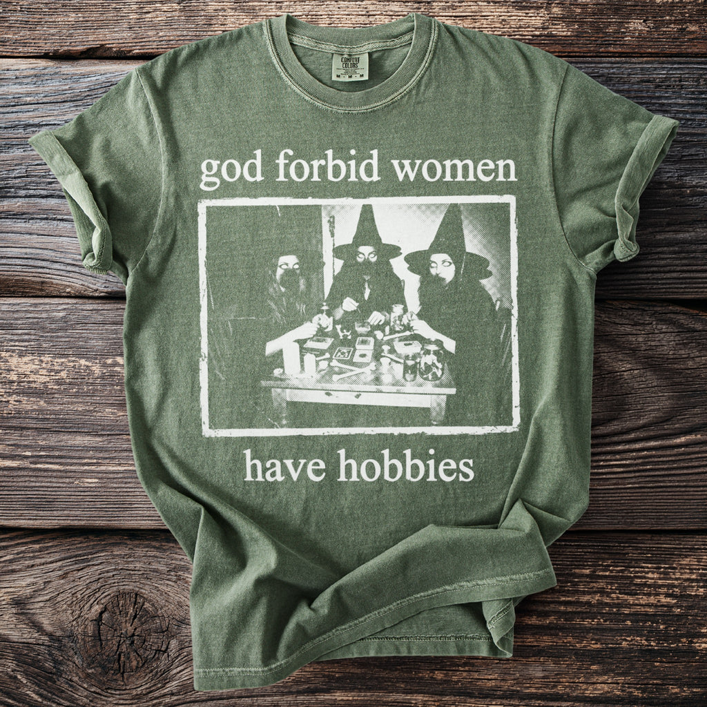 Green t-shirt with text "god forbid women have hobbies" and image of three people in witch hats.