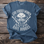 Blue t-shirt with white text: "God Forbid Women Have Hobbies" and moth graphic.