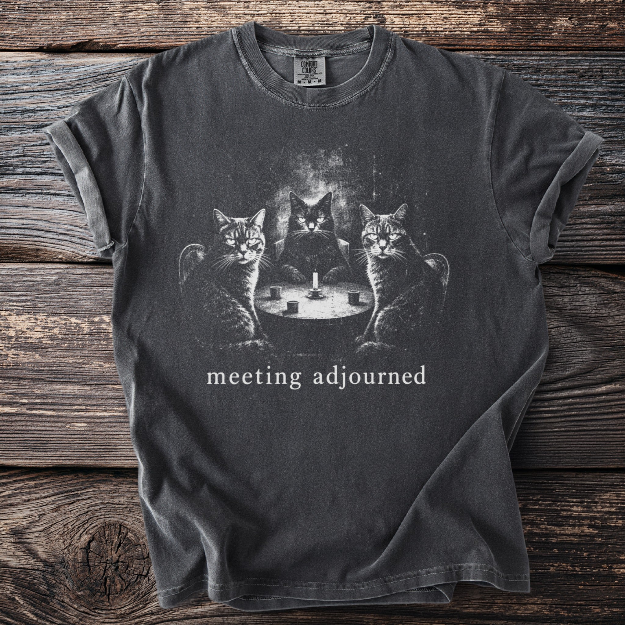 Dark t-shirt with three cats sitting around a table with a candle. "meeting adjourned" text.