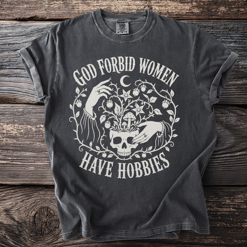 Dark grey t-shirt with white text "God Forbid Women Have Hobbies" and graphic.