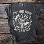 Dark grey t-shirt with white text "God Forbid Women Have Hobbies" and graphic.