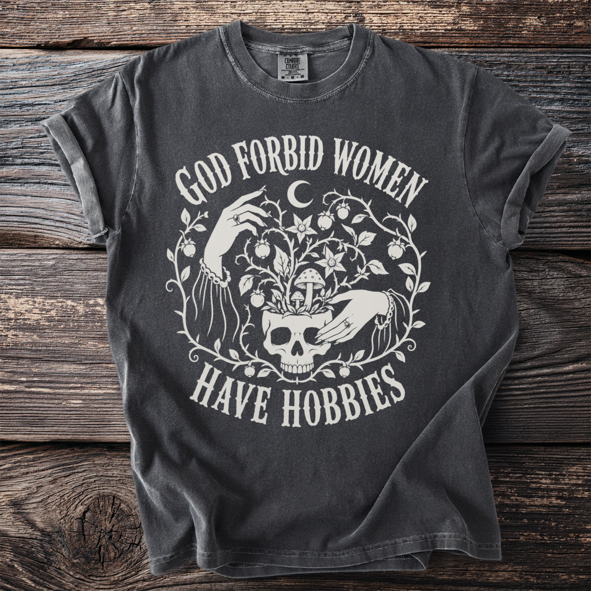Dark grey t-shirt with white text "God Forbid Women Have Hobbies" and graphic.