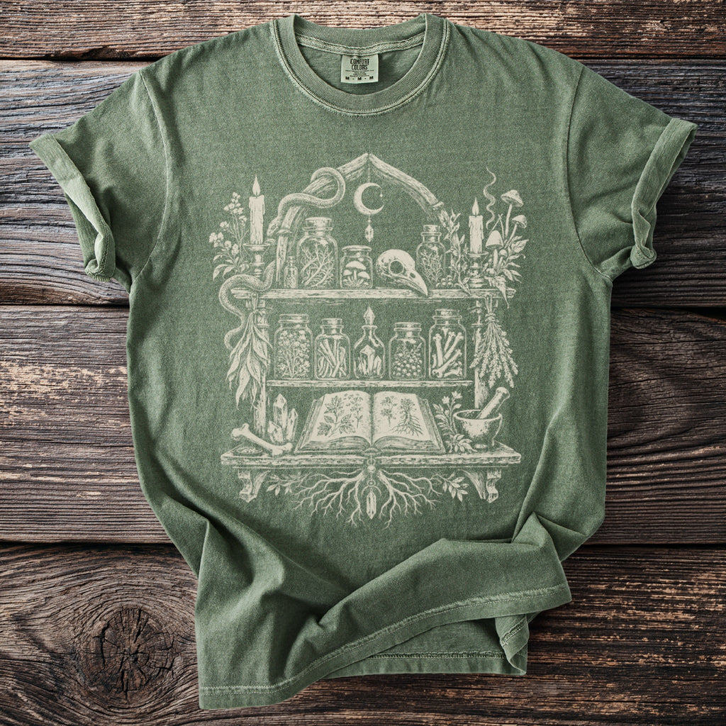 Green t-shirt with occult-themed graphic of shelves holding jars, a skull, and an open book.