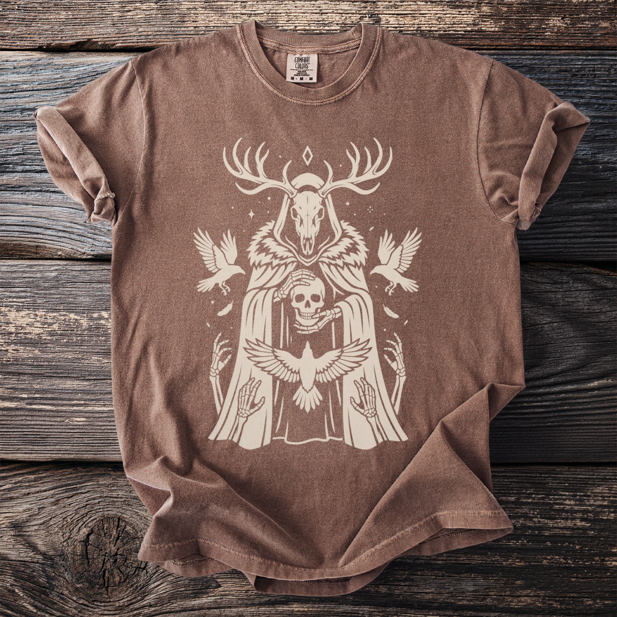 Brown t-shirt with a skull, skeleton hands, antlers, and birds graphic.