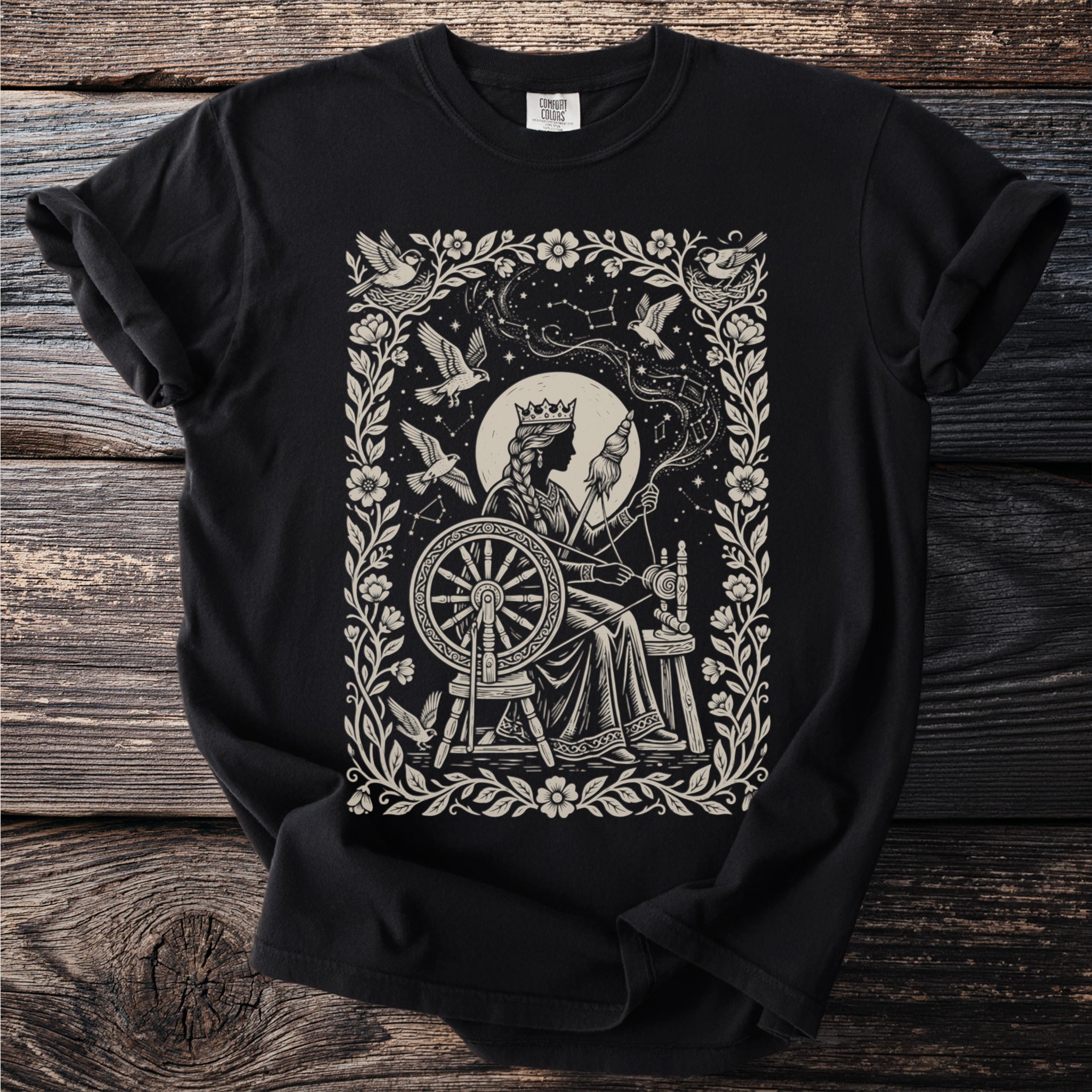 Black t-shirt with a queen at a spinning wheel surrounded by birds and constellations.