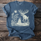 Blue t-shirt with a cream illustration of a raven, a fire, and a monstrous deer under a sun.