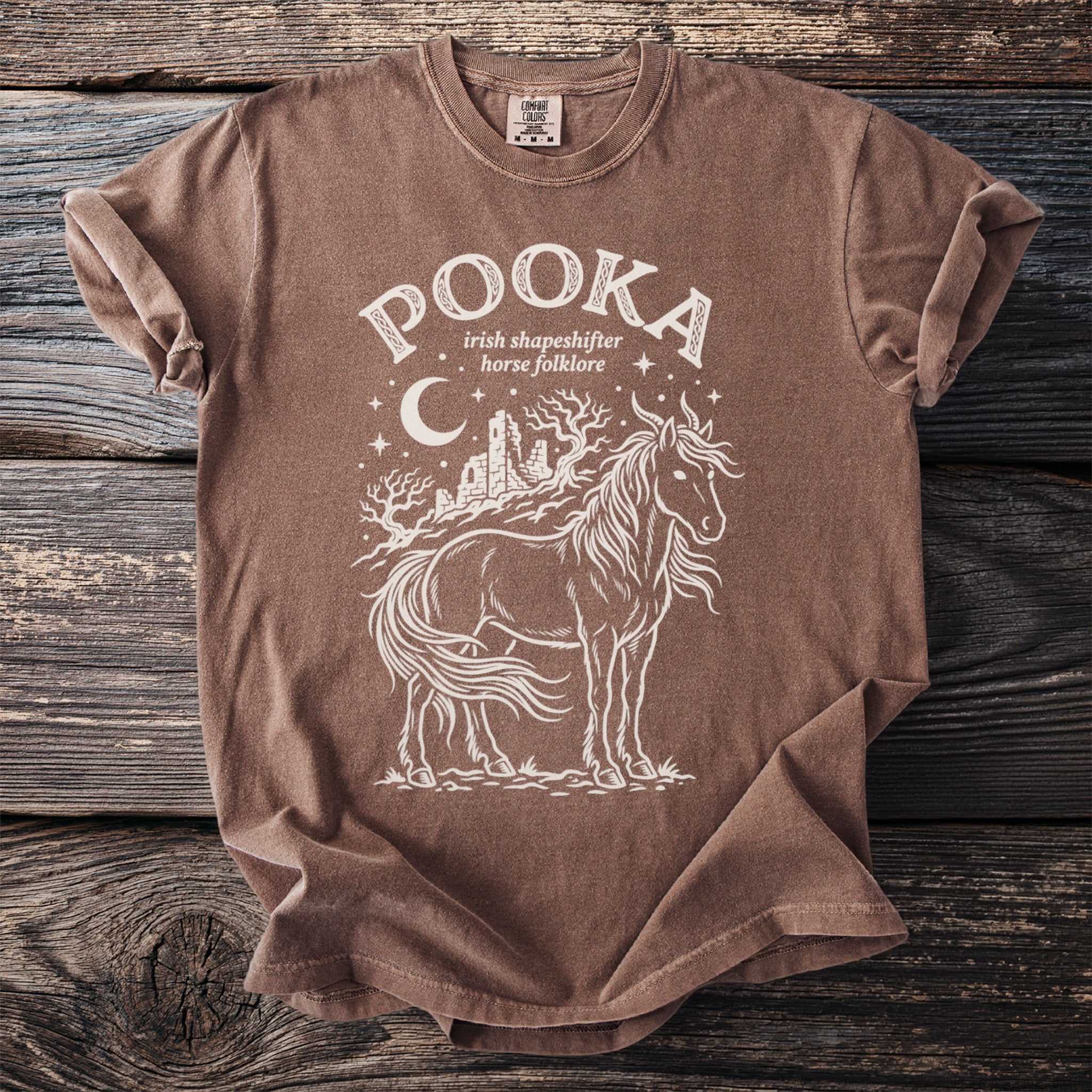 Brown t-shirt with cream graphic of a horse, castle ruins, trees, moon, and stars.