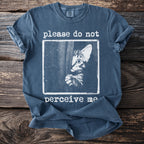 Blue t-shirt with a graphic of a shy cat and text "please do not perceive me".