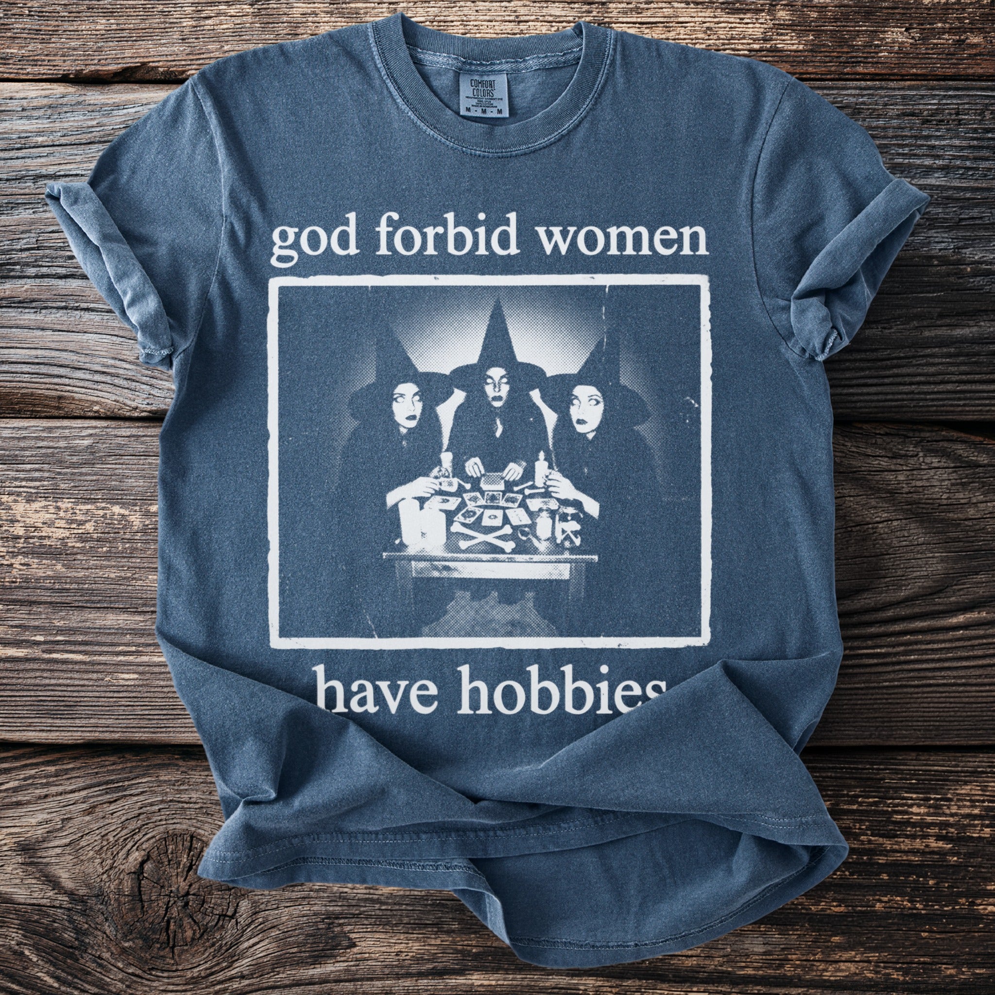 Blue t-shirt with graphic of three witches and text "god forbid women have hobbies".