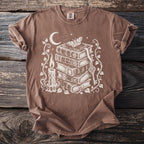 Brown t-shirt with a white graphic of books, candle, moon, key, and moth.